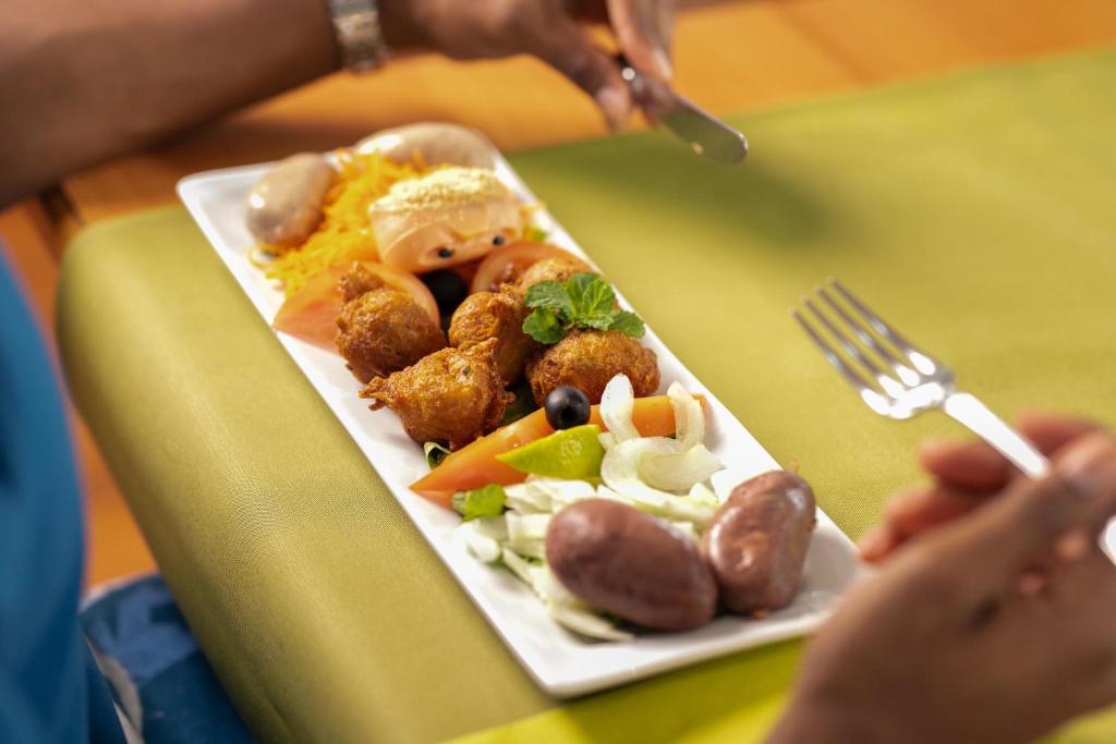 a plate of food on a table with a person holding a fork at Karibea Squash Hôtel in Fort-de-France