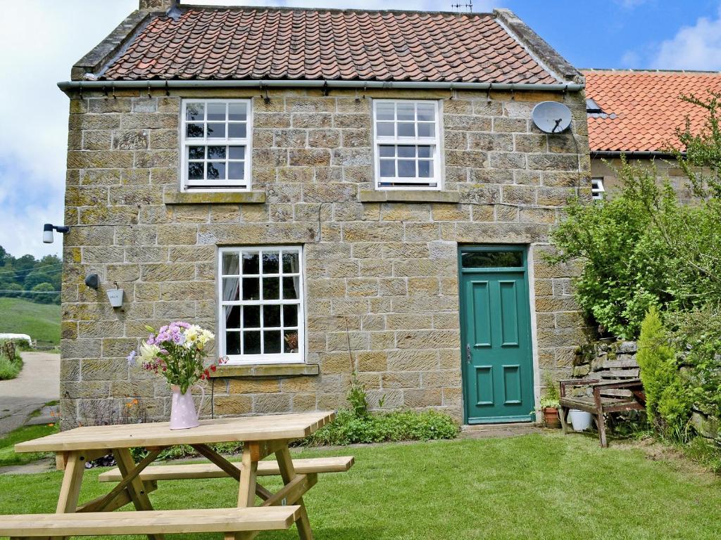 a picnic table in front of a stone house with a green door at Beckside Cottage in Fryup