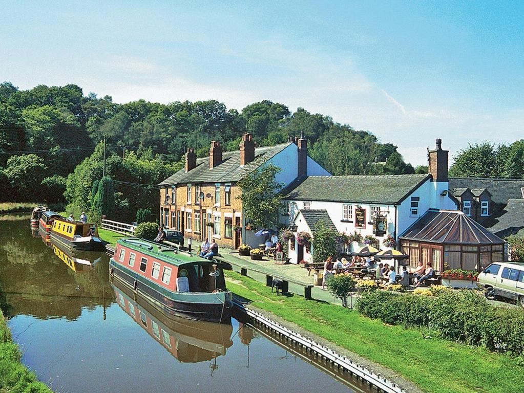 Ein Boot liegt in einem Fluss neben Gebäuden vor Anker. in der Unterkunft Hollybush Cottage - E2800 in Cheddleton