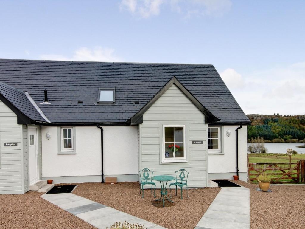 a white house with a black roof and two chairs at Kestrel Cottage - 27937 in Cambusbarron