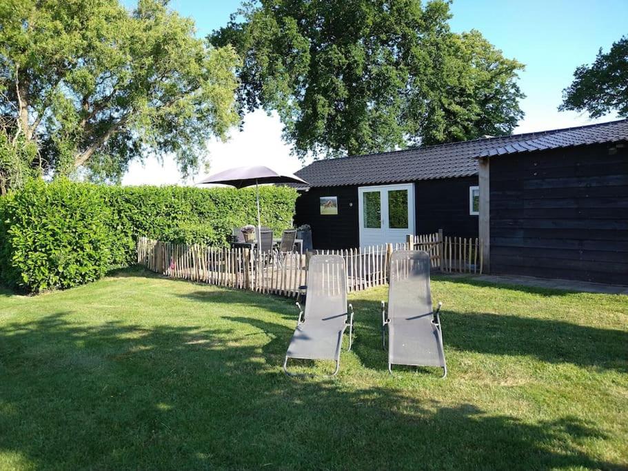 two lawn chairs and an umbrella in a yard at Linderhuisje, rust, ruimte, privacy en natuur in Linde