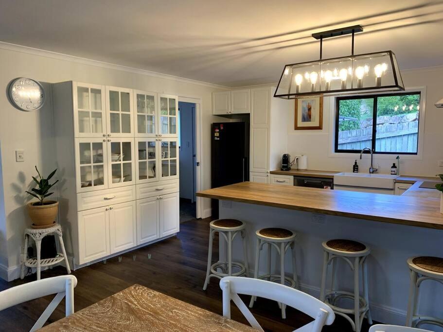 une cuisine avec des placards blancs et un îlot avec des tabourets de bar dans l'établissement Fig Street Cottage, à Maleny