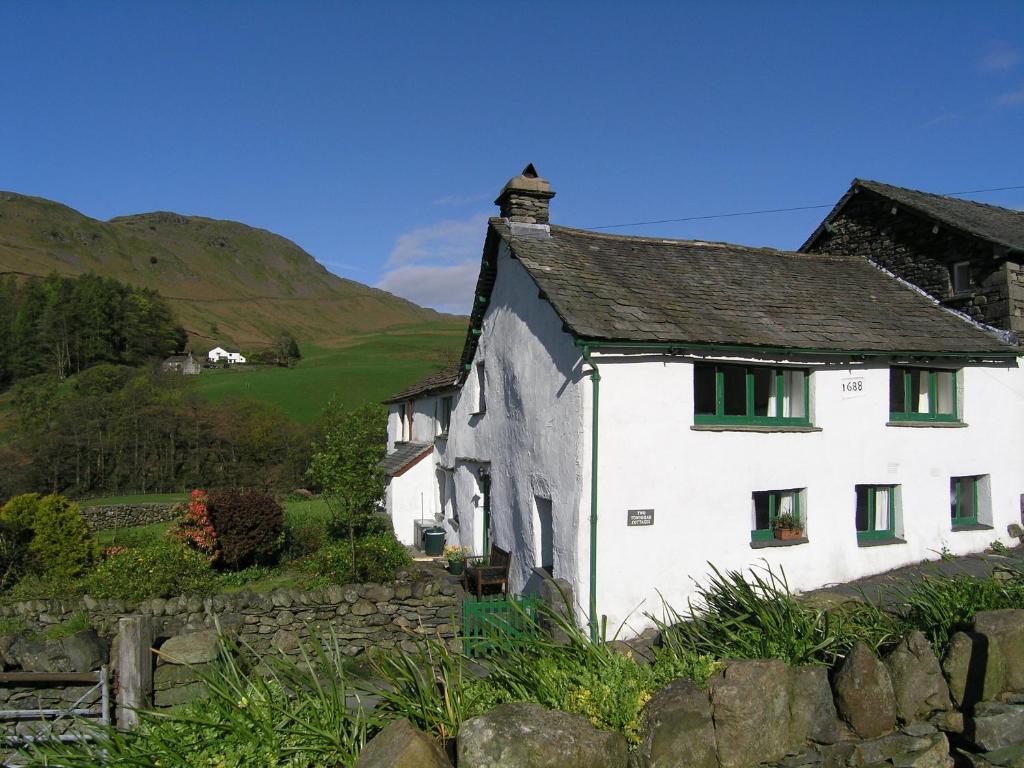 a white house with green windows in a field at 2 Town Head Cottages in Grasmere