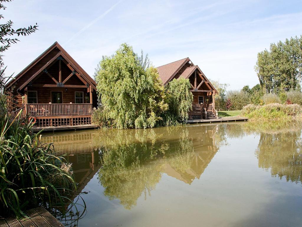 a log cabin on a lake with its reflection in the water at Kingfisher Lodge - E4159a in Miningsby