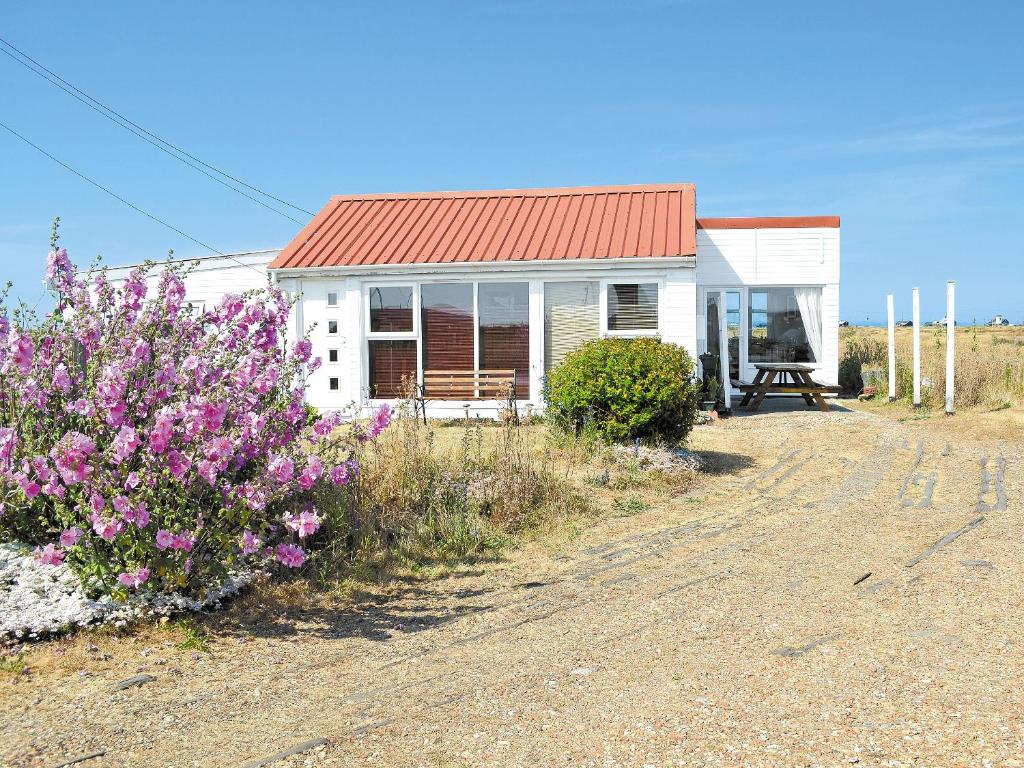 a white house with a red roof and some flowers at Les Quatre Vents in Dungeness