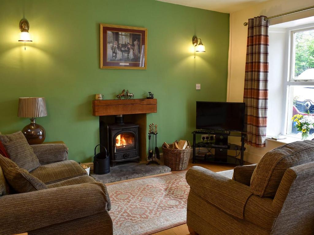a living room with green walls and a fireplace at Coach House Cottage in Buckden
