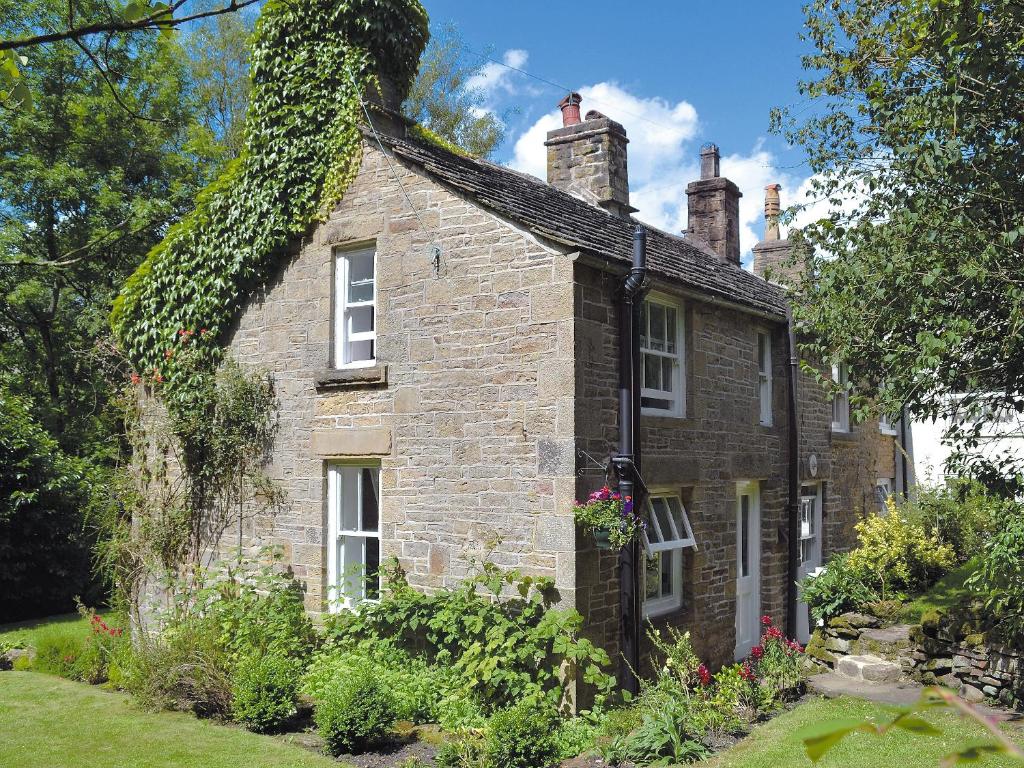 an old stone house with ivy growing on it at Drum And Monkey Cottage in Chapel en le Frith