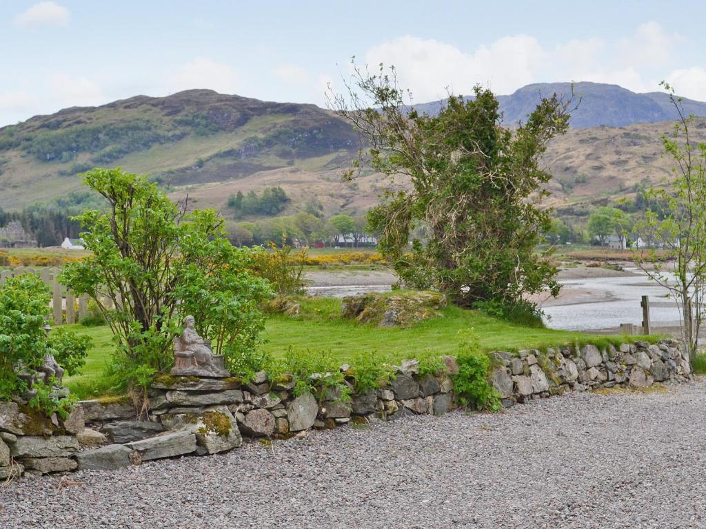 a stone wall with trees and mountains in the background at Rams Cottage in Glenelg