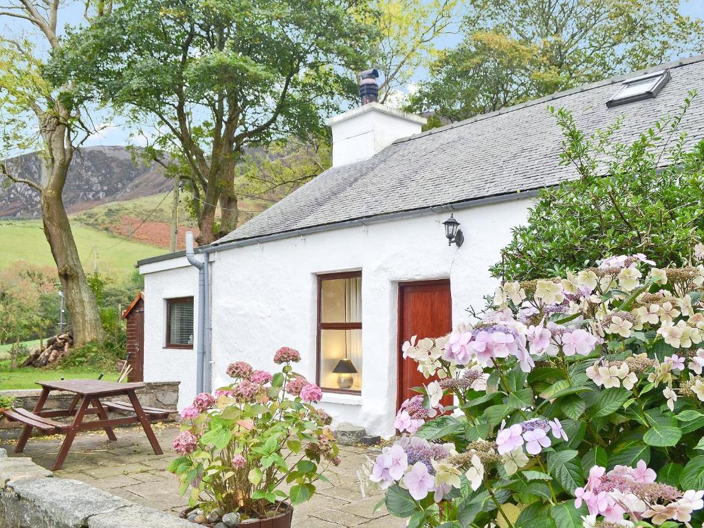 a white cottage with a picnic table and flowers at Llwyn Y Brig Isaf in Trevor