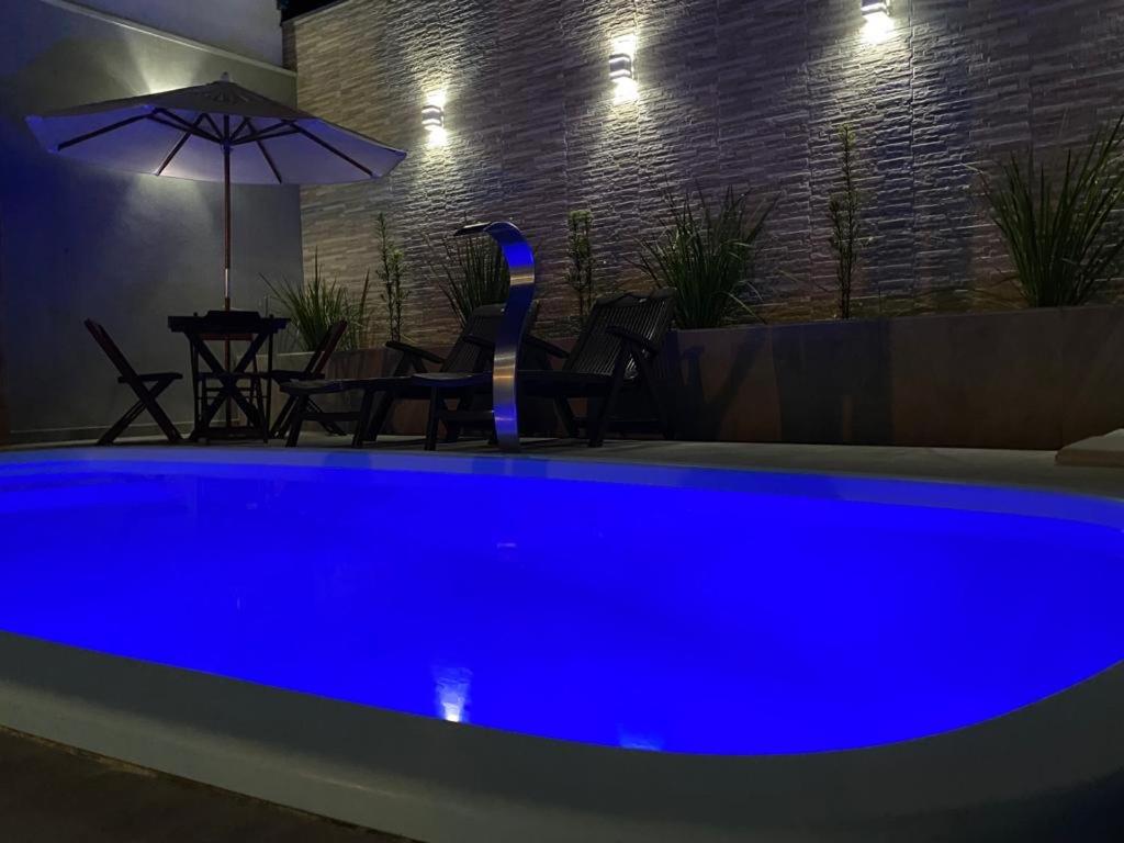 - une piscine bleue la nuit avec une table et un parasol dans l'établissement Casa com piscina e um quarto com ar split pé na areia a 50 metros da praia, à Prado