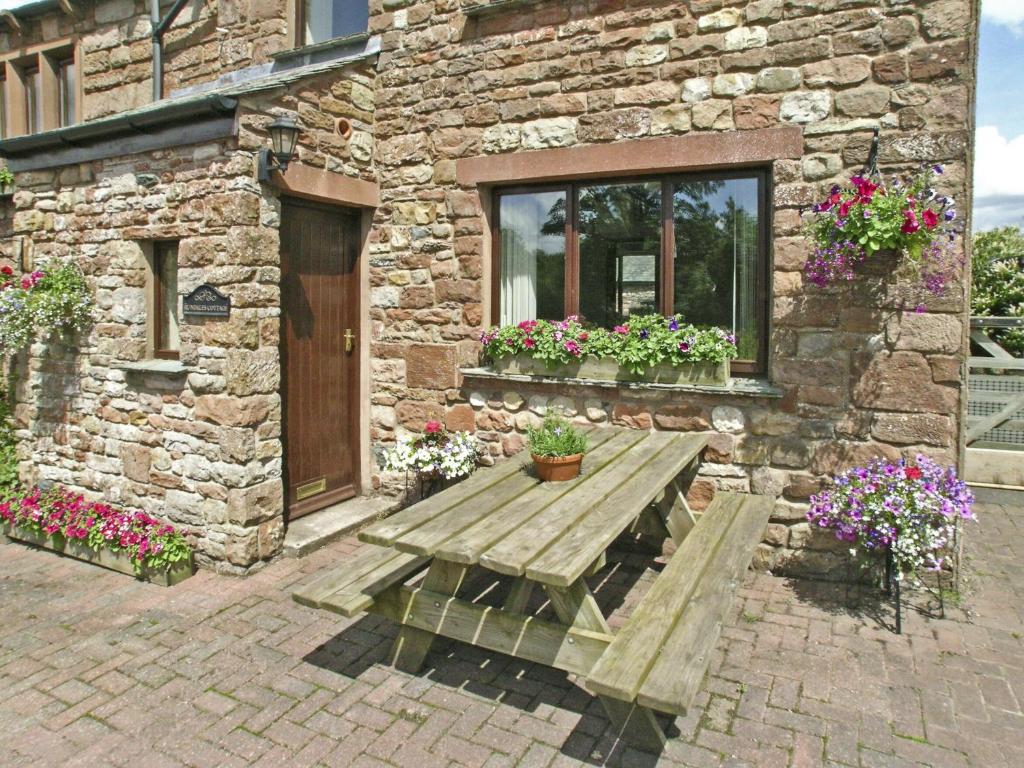 a wooden bench sitting outside of a building with flowers at Rundales Cottage in Appleby