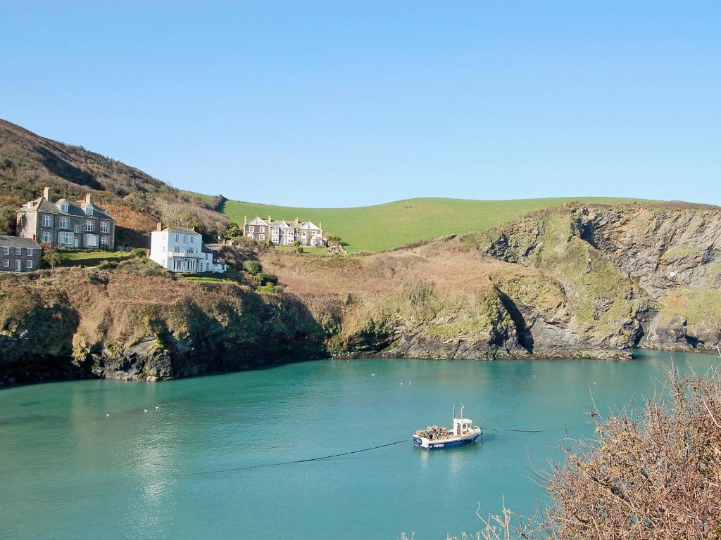 a boat in a body of water with houses on a hill at Mainbrace in Port Isaac