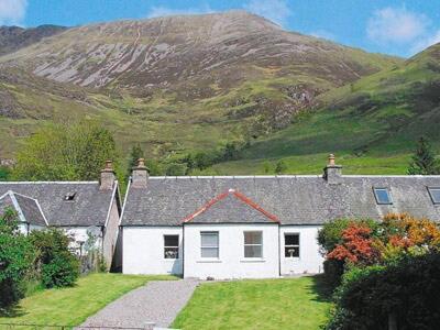 a white house with a mountain in the background at Brightwater Cottage in Arnisdale