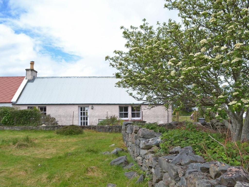 a white house with a stone wall and a tree at The Cottage in Duirinish