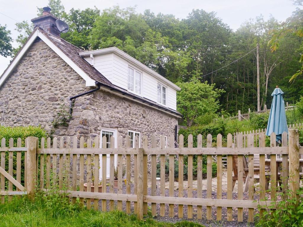 an old stone house with a wooden fence and an umbrella at Caeberllan in Llanfair Caereinion