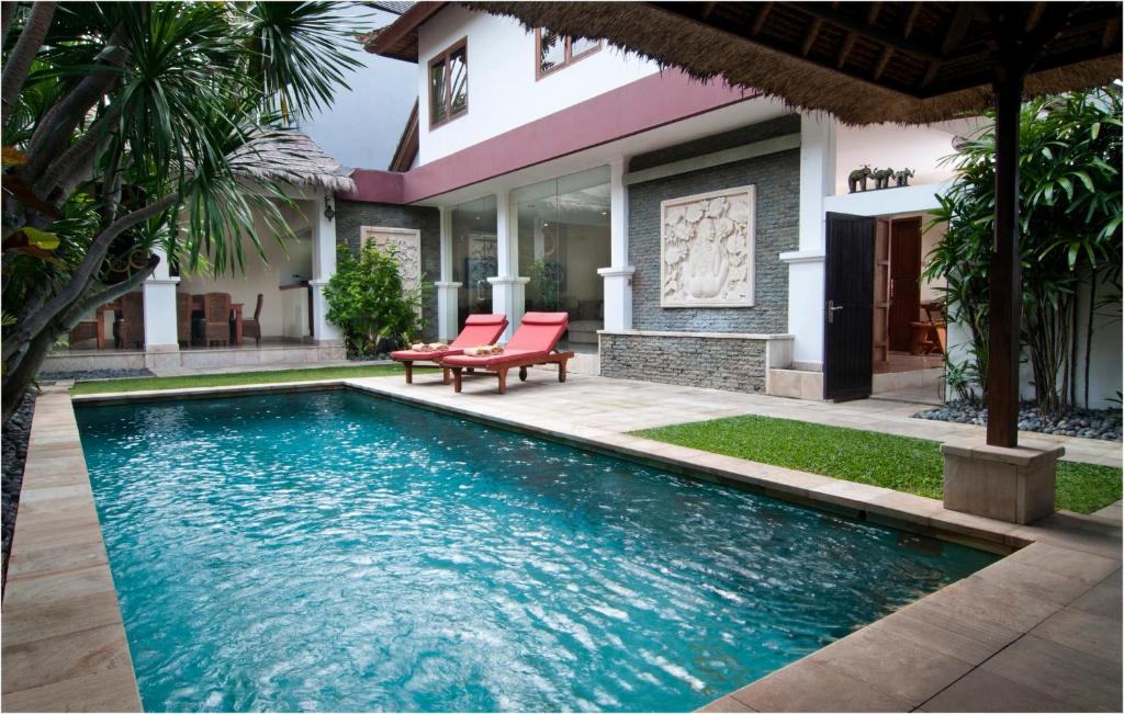 a swimming pool in front of a house with two red chairs at 6BR Villa Sensel - Minggu Villas Seminyak in Seminyak