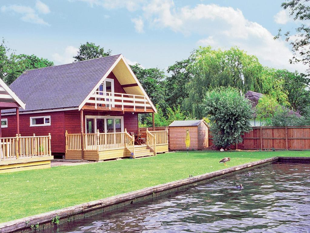 uma casa vermelha com um deque e uma massa de água em The Wherry em Wroxham