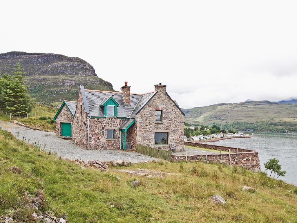 una casa de piedra en una colina junto a un cuerpo de agua en Rubha Lodge, en Shieldaig