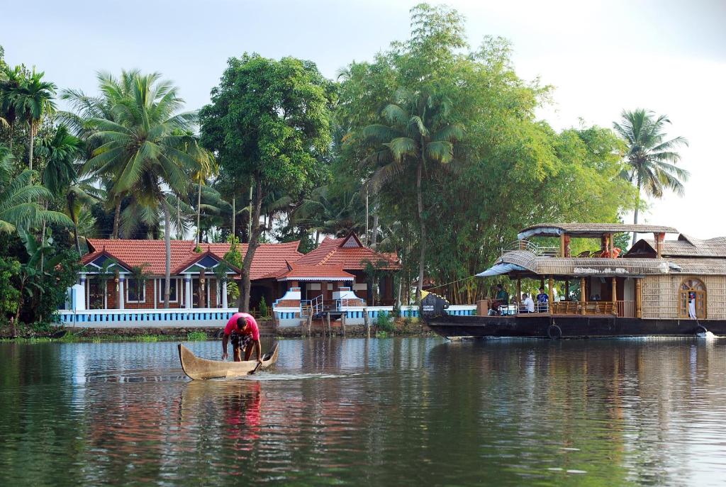 a person in a boat on a river with a house at The Lake by Maat Hotels in Alleppey