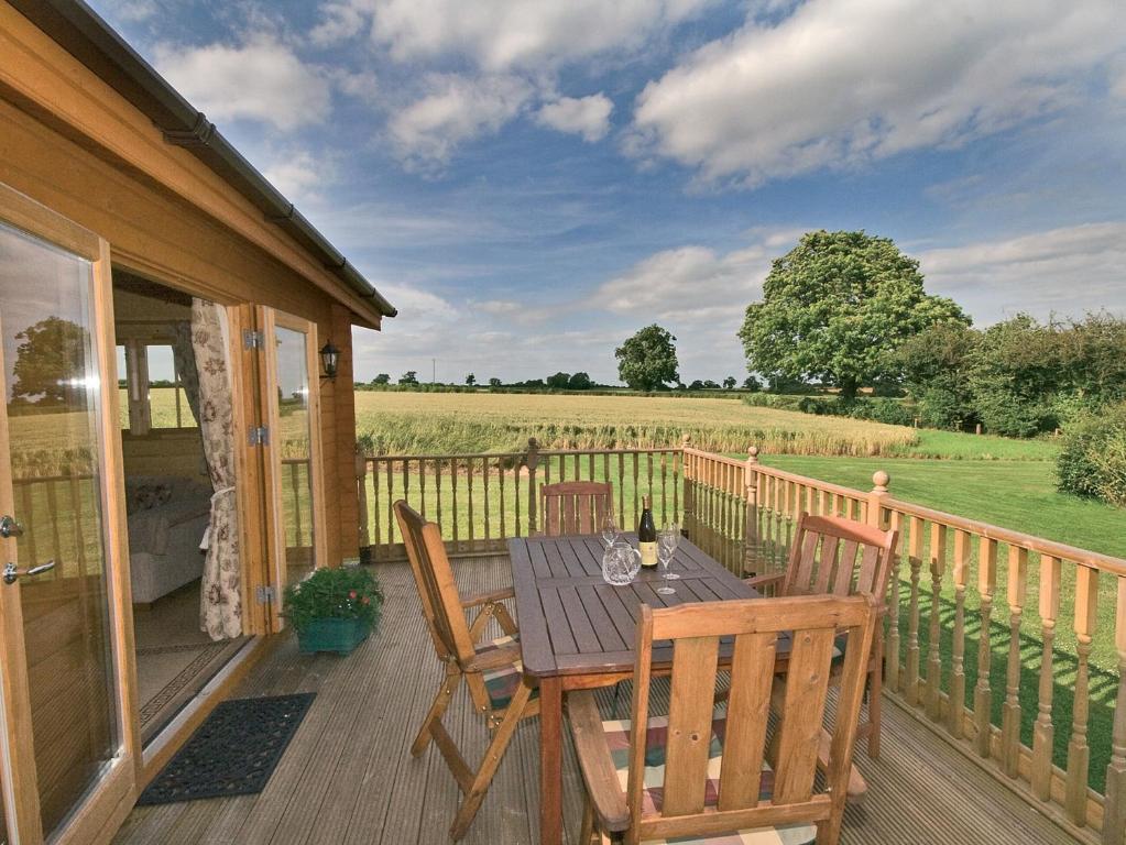 une terrasse en bois avec une table, des chaises et un champ dans l'établissement Field Lodge - E4380, à Overseal