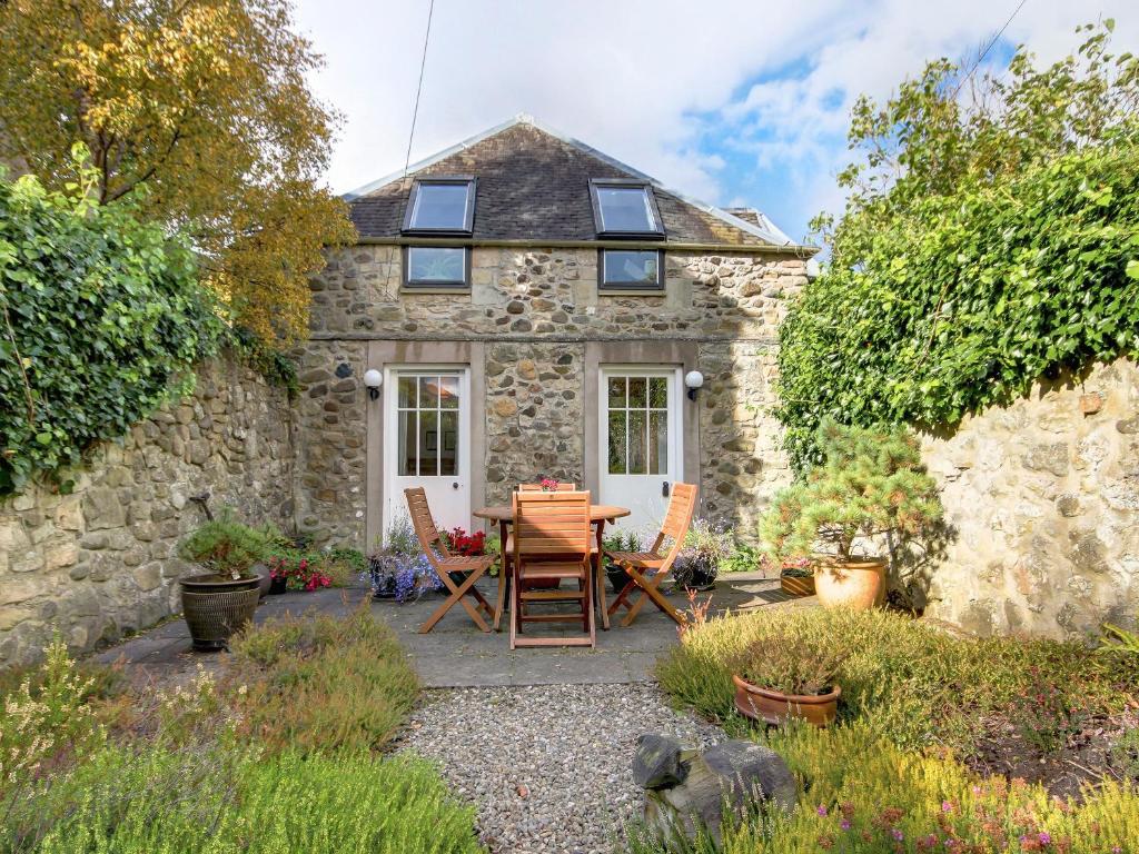 Cabaña de piedra con mesa y sillas frente a ella en Garden Cottage, en Linlithgow