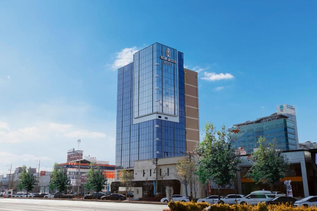 un edificio de cristal alto con coches estacionados frente a él en Daegu Billion Western Hotel en Daegu