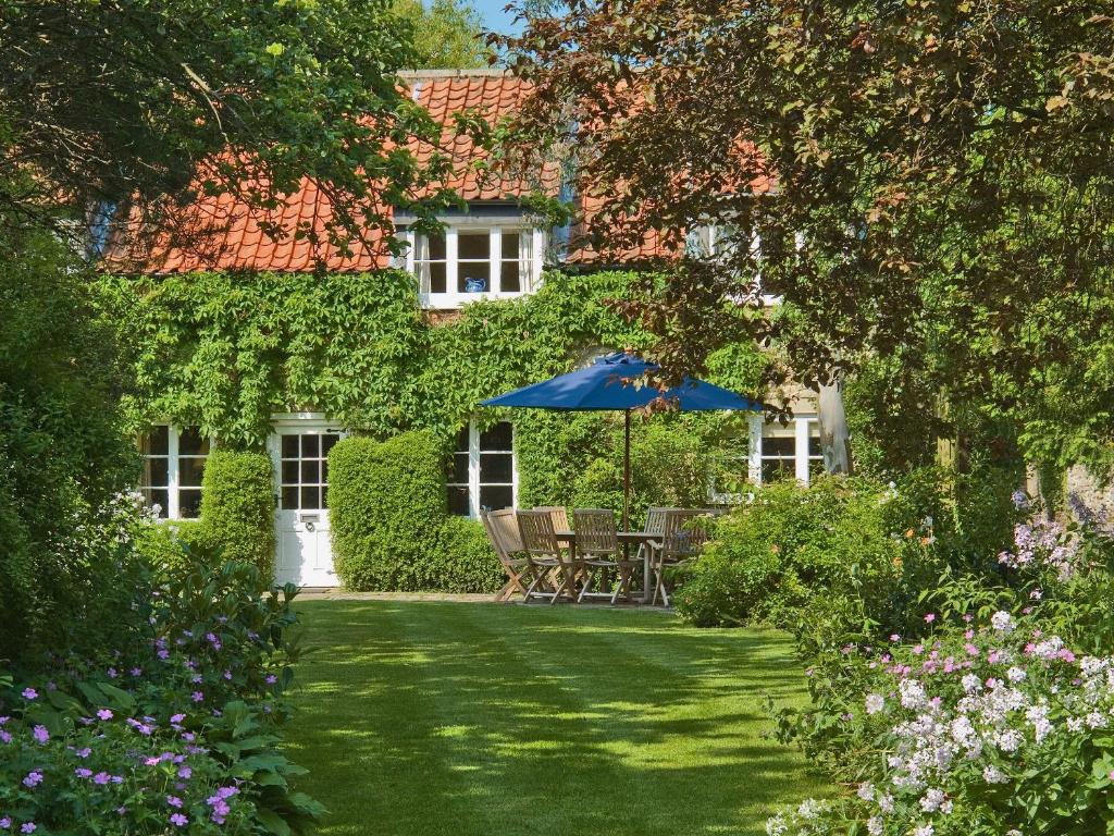 a garden with a table and an umbrella in front of a house at Hungate Garden Cottage in Pickering