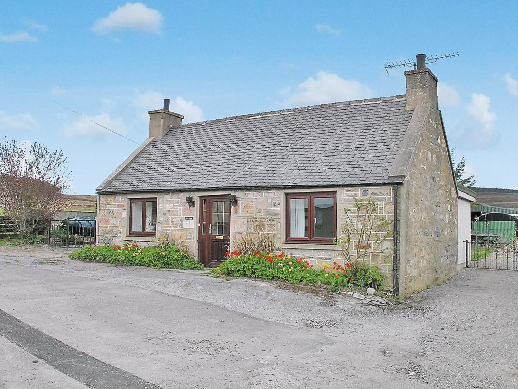 a small brick house with flowers in front of it at Honey Cottage in Auchnarrow