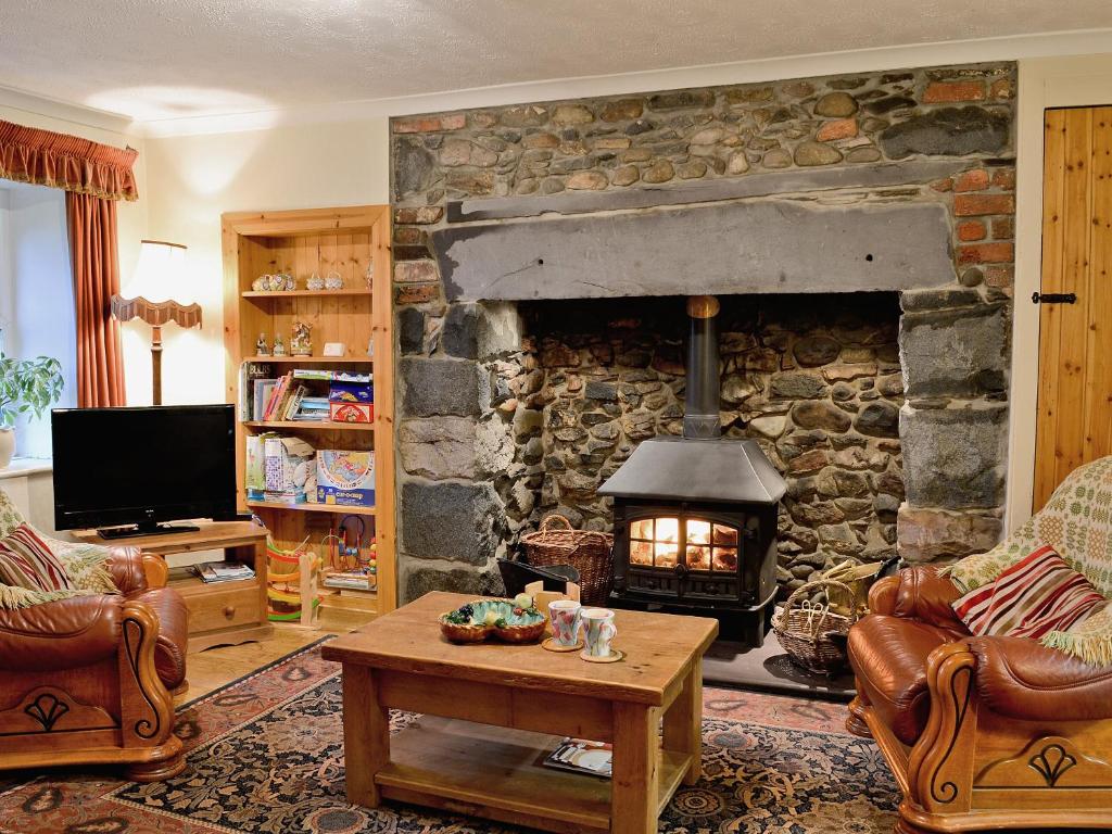 a living room with a stone fireplace with a stove at Is Helen Cottage in Caernarfon