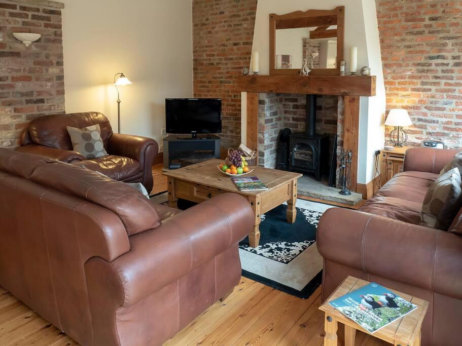 sala de estar con muebles de cuero y chimenea en Wheelhouse Cottage . A brick-built barn conversion, en Thirsk
