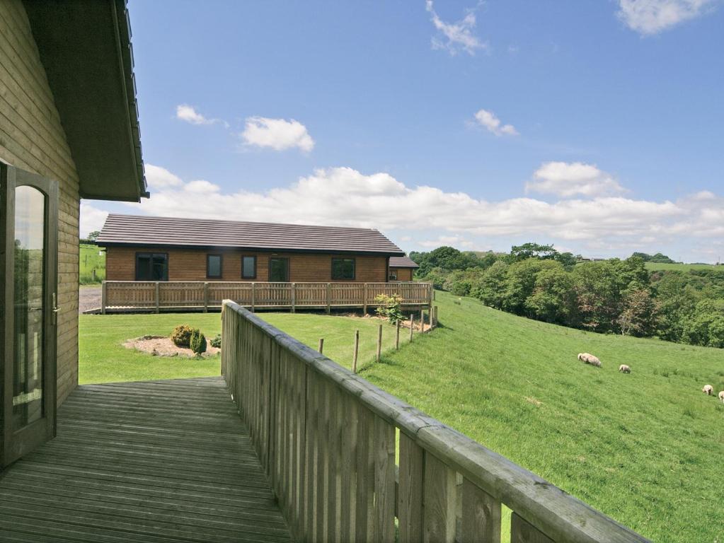 a house with a wooden porch and a field with sheep at Woodside Lodge - Hw7520 in Penybont