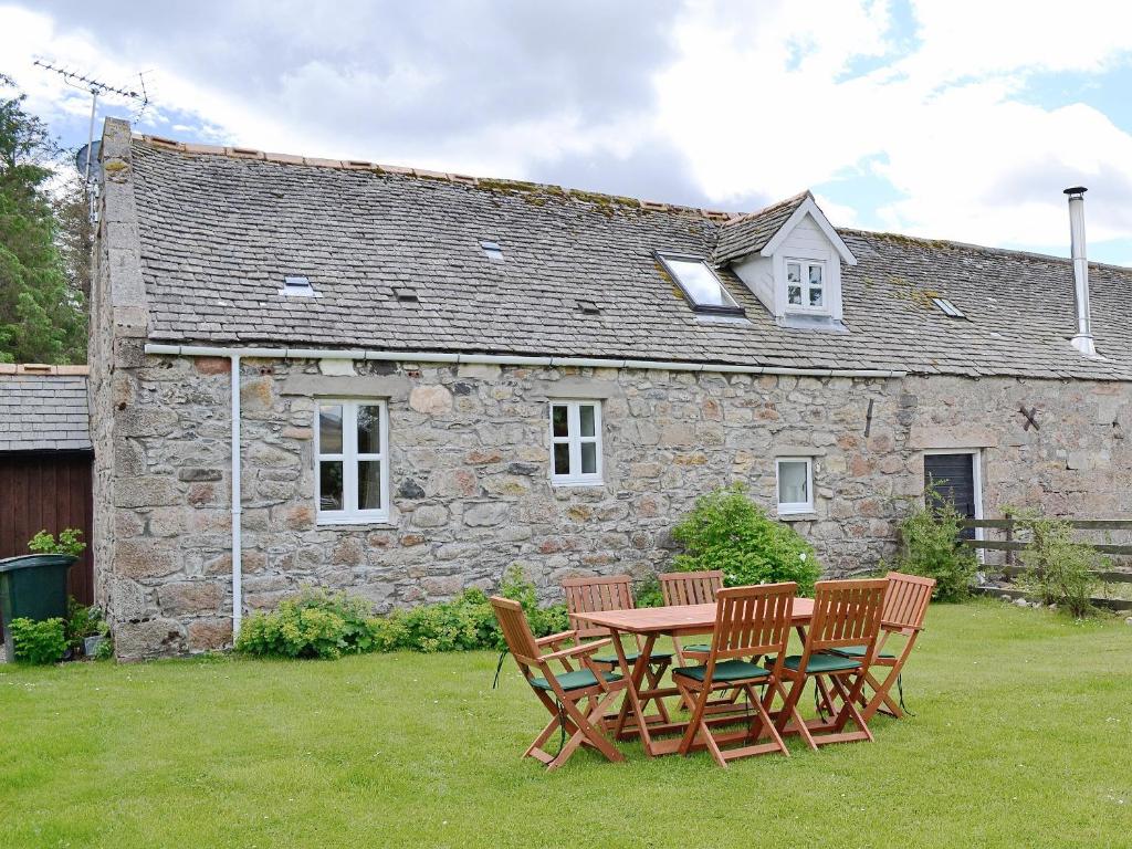 uma mesa e cadeiras em frente a uma casa de pedra em Woodside Cottage em Auchnastank