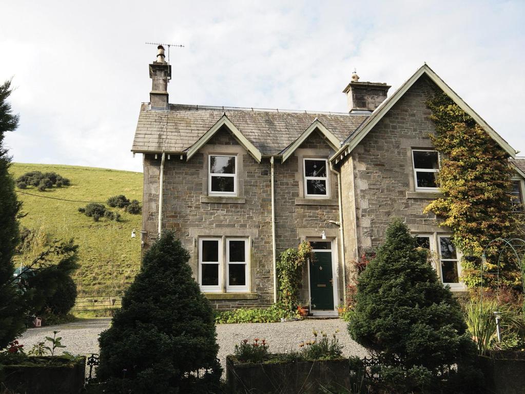 a stone house with a green hill in the background at Ewes Schoolhouse in Bentpath