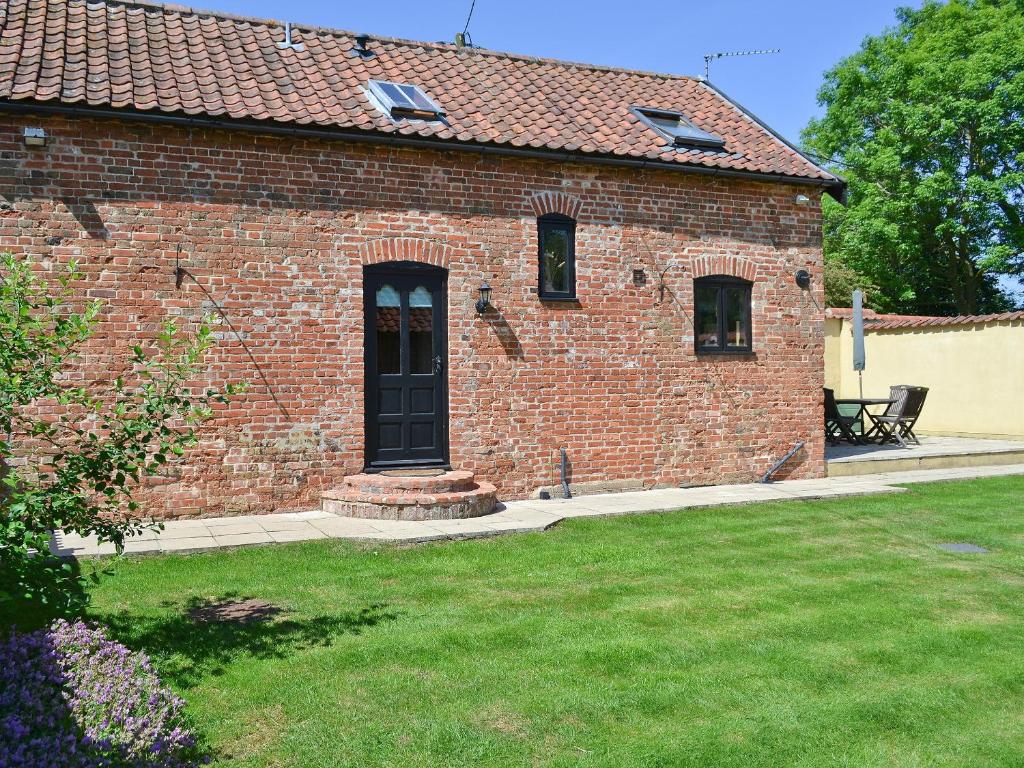 een stenen huis met een zwarte deur en een tuin bij The Cottage in Great Ellingham