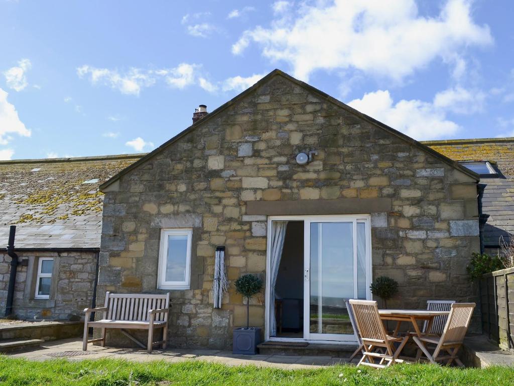 Cabaña de piedra con mesa y sillas frente a ella en Limpet Cottage, en Boulmer