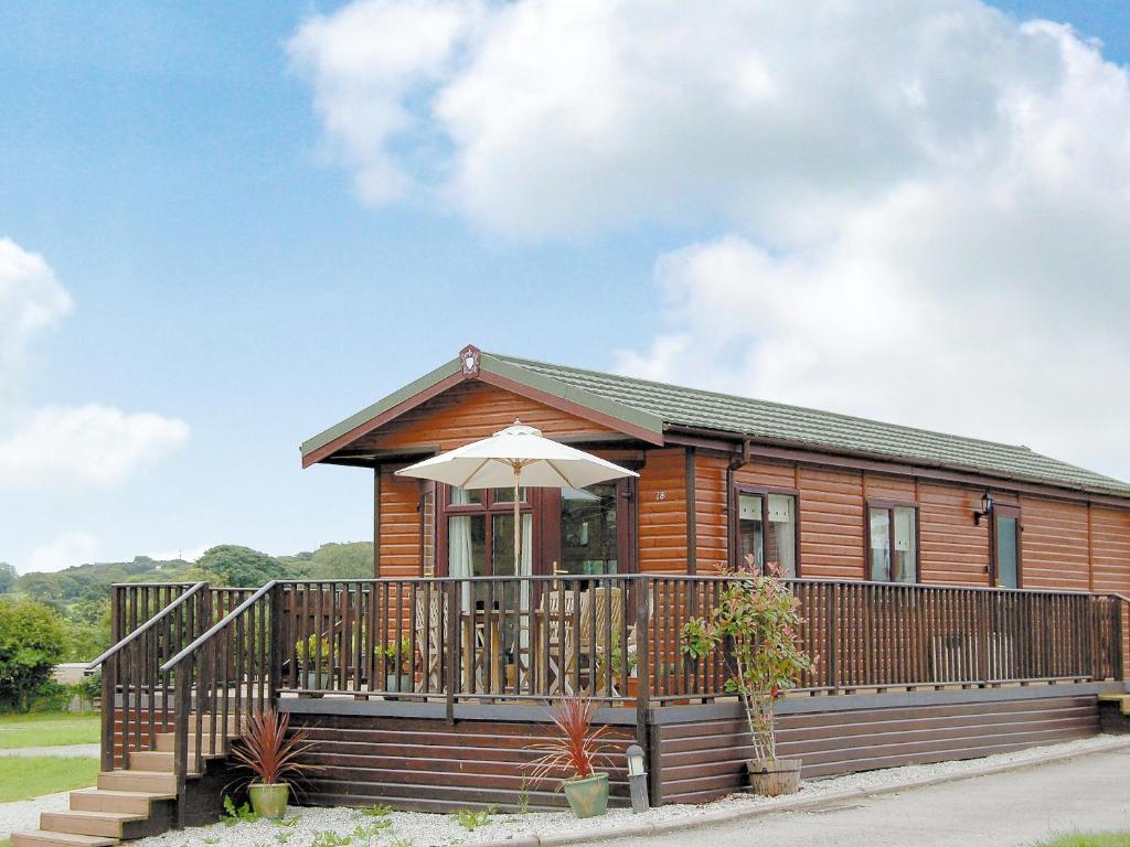 a log cabin with a deck and an umbrella at Rosewater Lodge in Saint Teath