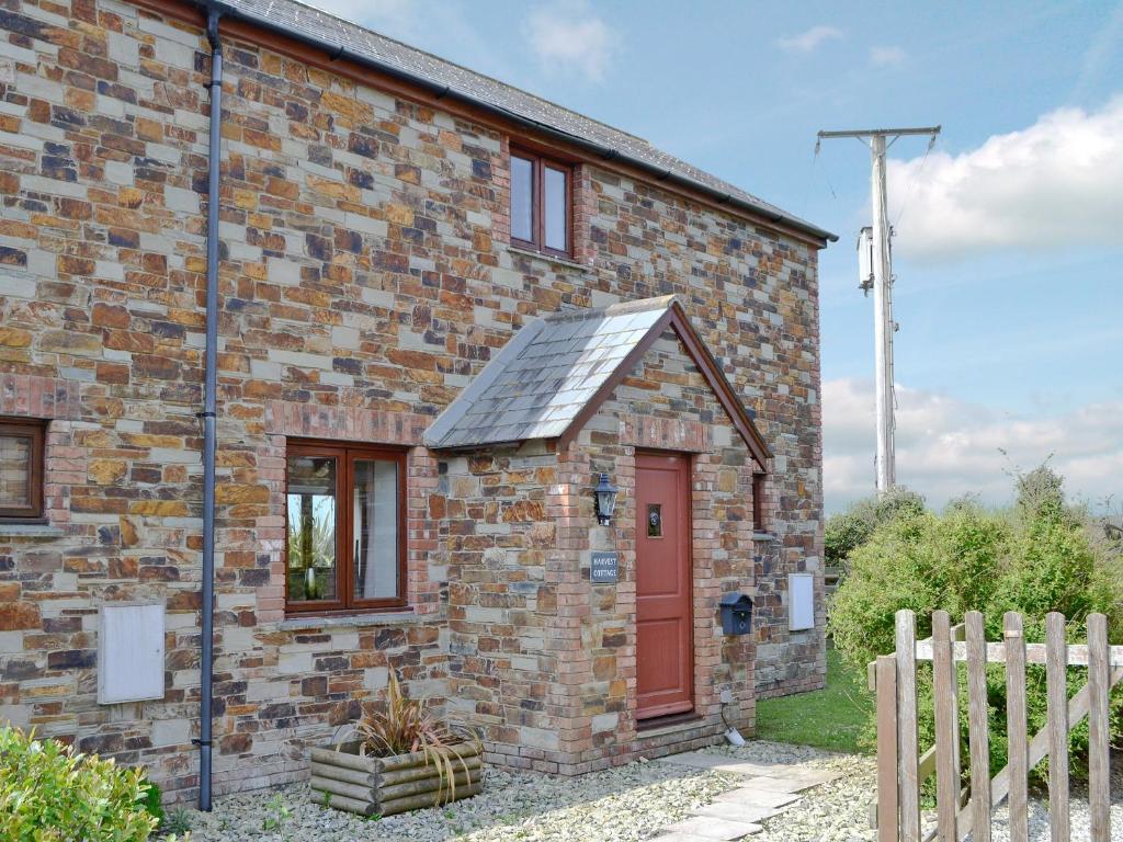 une maison en briques avec une porte rouge et une clôture dans l'établissement Harvest Cottage, à Padstow