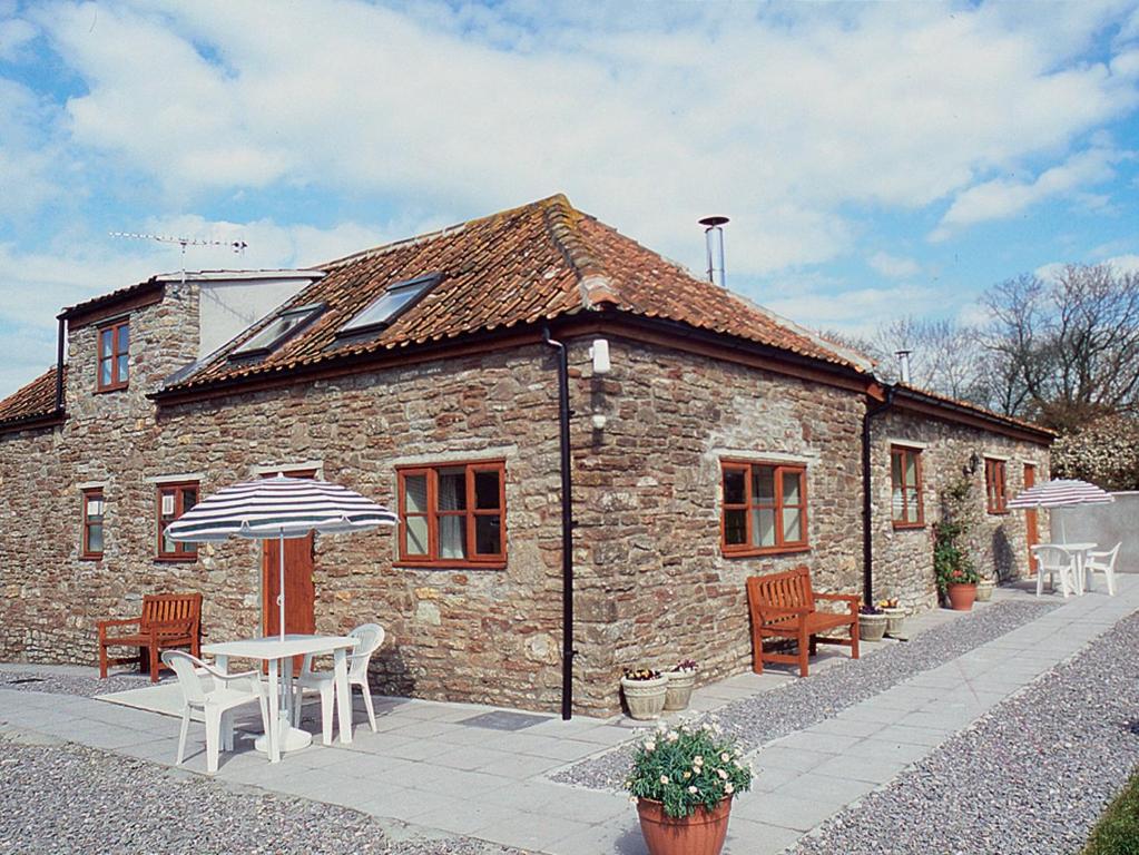 une maison en pierre avec une table, des chaises et un parasol dans l'établissement Challeys Cottage - E2378, à Banwell
