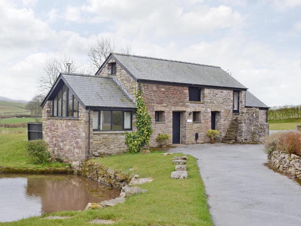 a stone house with a pond in front of it at TY NANT-oxl in Gwynfe