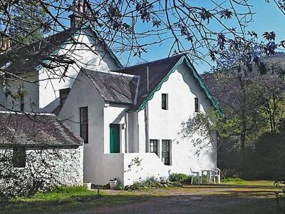 biały budynek z czarnym dachem i zielonymi drzwiami w obiekcie Glencoe Cottage w mieście Glencoe