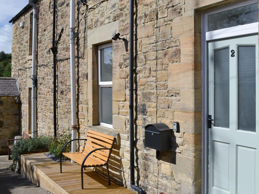 a bench sitting on a wooden deck next to a brick building at Oake Cottage in Warkworth