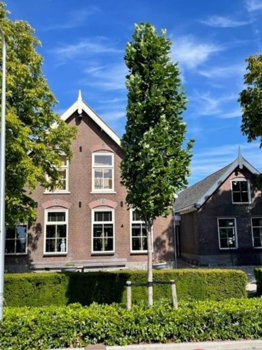 een groot bakstenen huis met een boom ervoor bij Boutique appartement vlak bij Amsterdam in Rijnsaterwoude