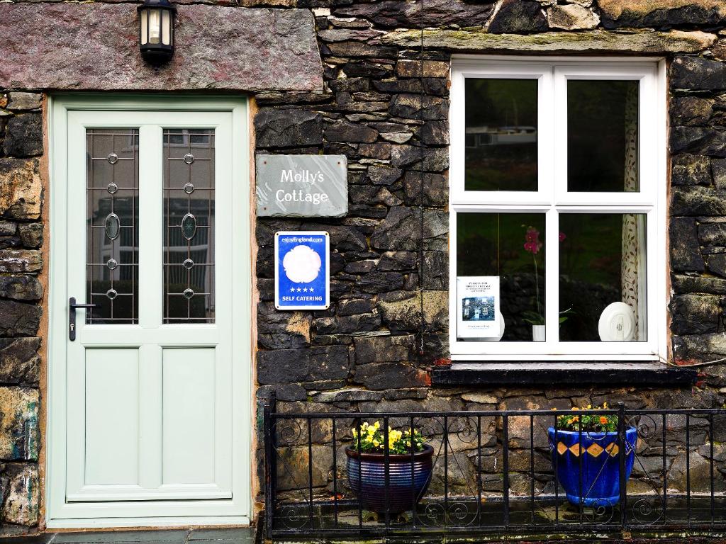 a stone building with a white door and two windows at Mollys Cottage in Glenridding