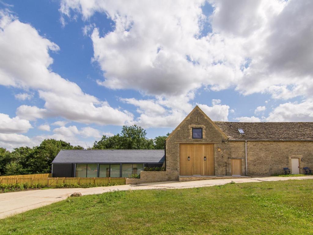 an old stone building with a wooden garage at The Cotswold Barn in Ampney Crucis