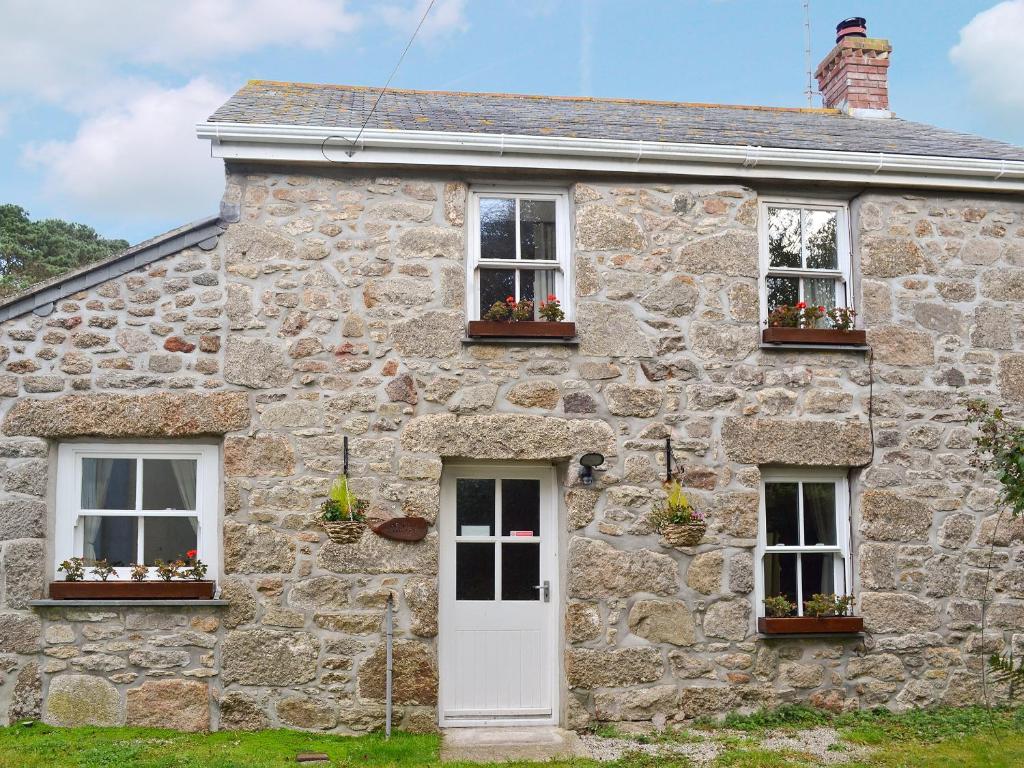 una antigua casa de piedra con dos ventanas y una puerta blanca en Meadow Cottage en St Just