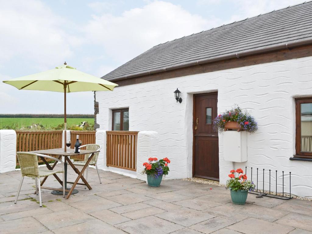 a patio with a table and an umbrella and a house at Bwthyn Bach - 29177 in Trelech