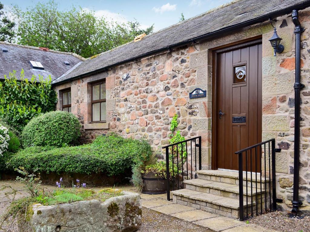 an old stone house with a wooden door and stairs at Busy Lizzie Cottage-mfo in Akeld
