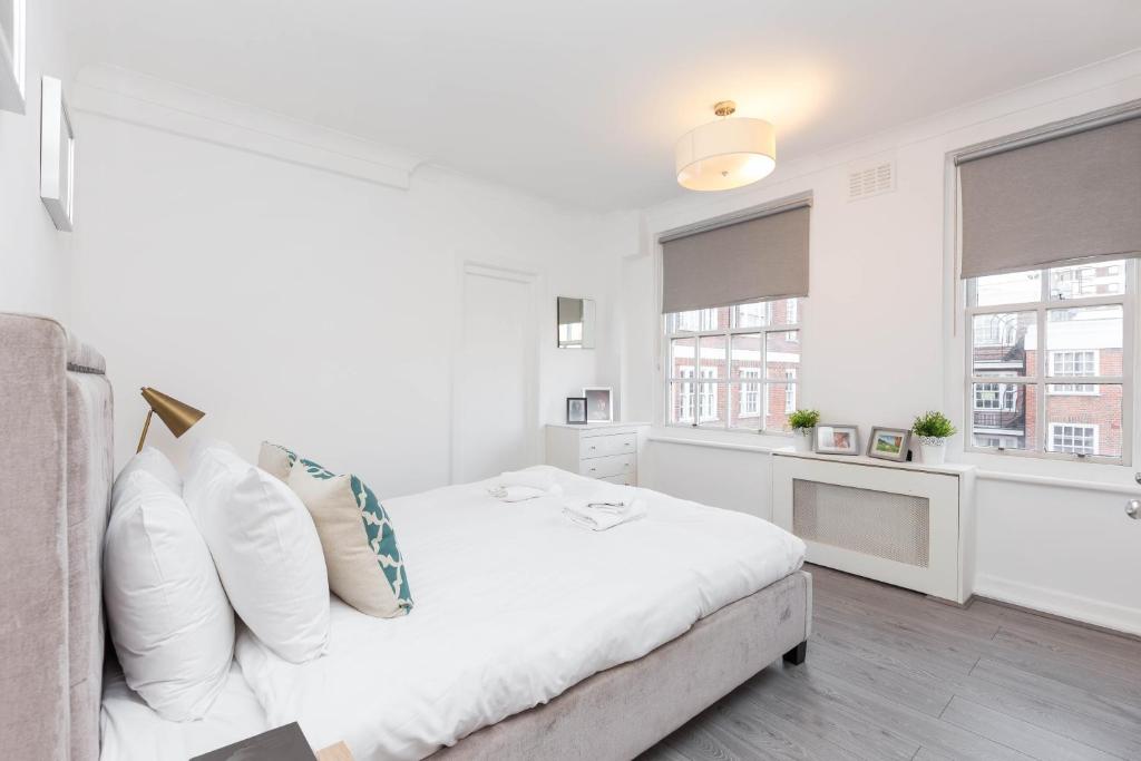 a white bedroom with a bed and two windows at Urban Hyde Park One-Bedroom Retreat in London
