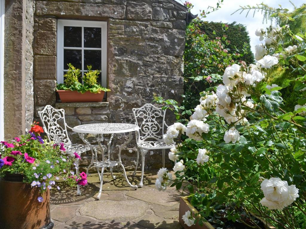 a patio with two chairs and a table and flowers at Rose Cottage - Lpd in Ireby