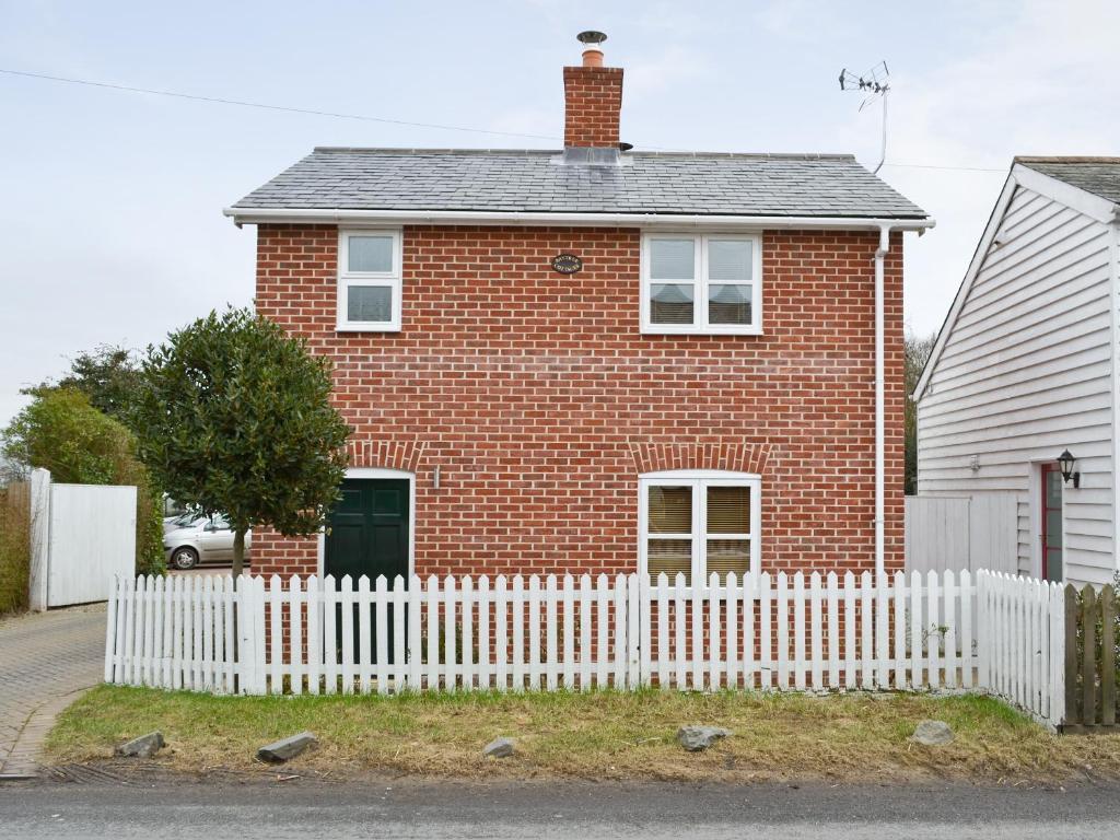 uma casa de tijolos vermelhos com uma cerca branca em Baytree Cottage 1 em Birch
